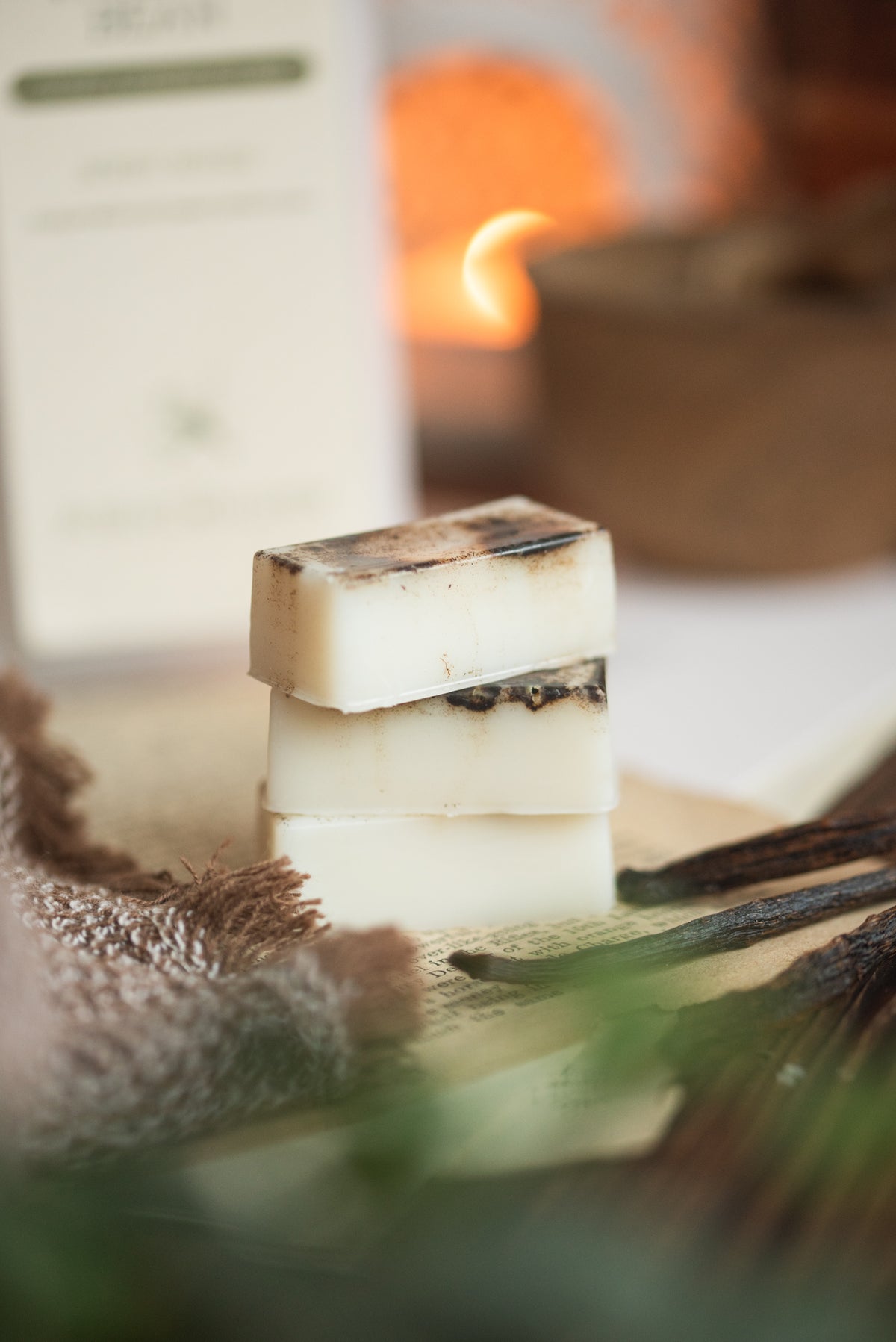 Three stacked rectangular wax melts on a wooden surface with a blurred background and vanilla pods