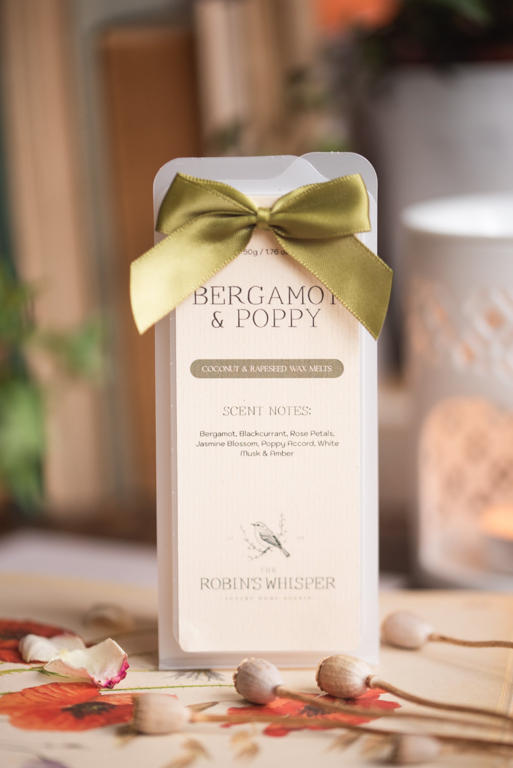 Product packaging with a moss green bow labelled 'Bergamot & Poppy' on a blurred background.
