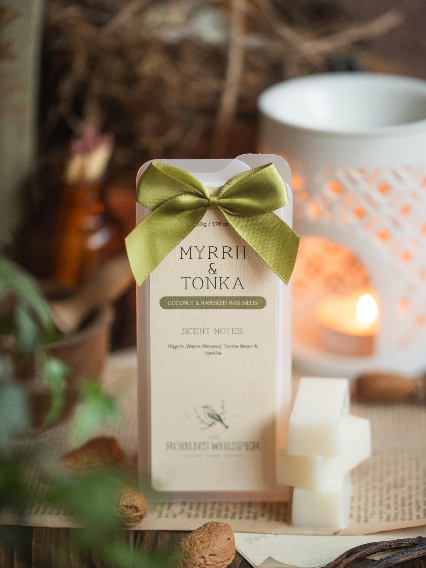 Myrrh & Tonka wax melt bar with a green bow on a wooden surface with a wax burner in the background.