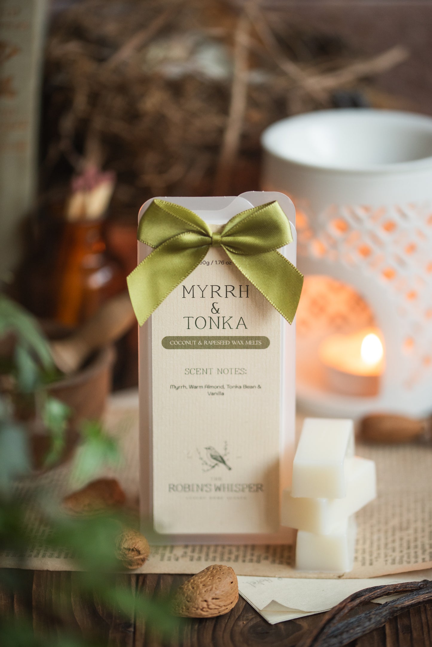 Myrrh & Tonka wax melt bar with a green bow on a wooden surface with wax burner and plants.