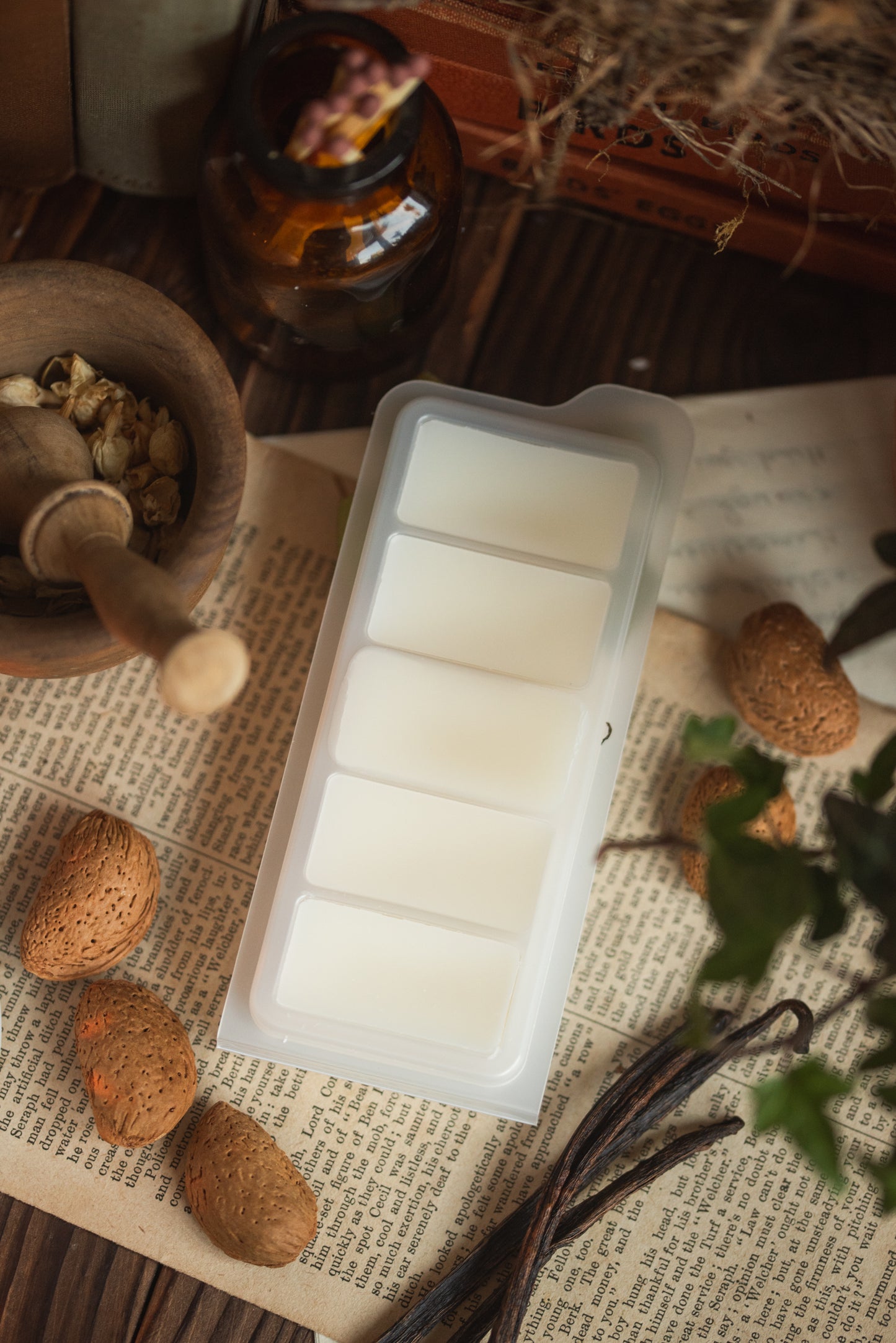 Rectangular clamshell with white wax bars on a rustic surface with almonds and vanilla pods.